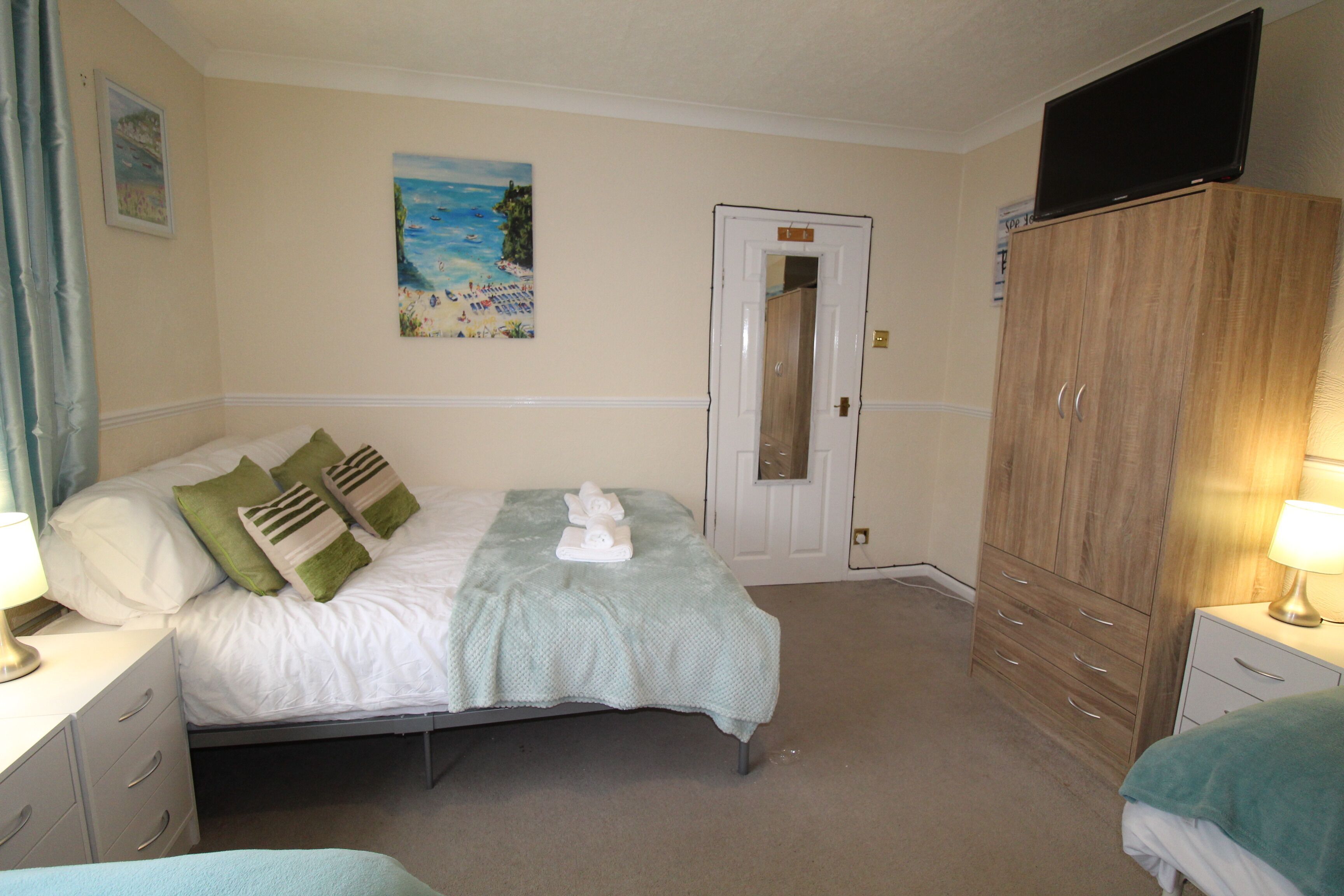A bedroom with a bed, a wardrobe, a television, and a painting on the wall.