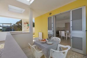 Un balcon avec une table dressée pour le dîner, des chaises blanches et un mur jaune.