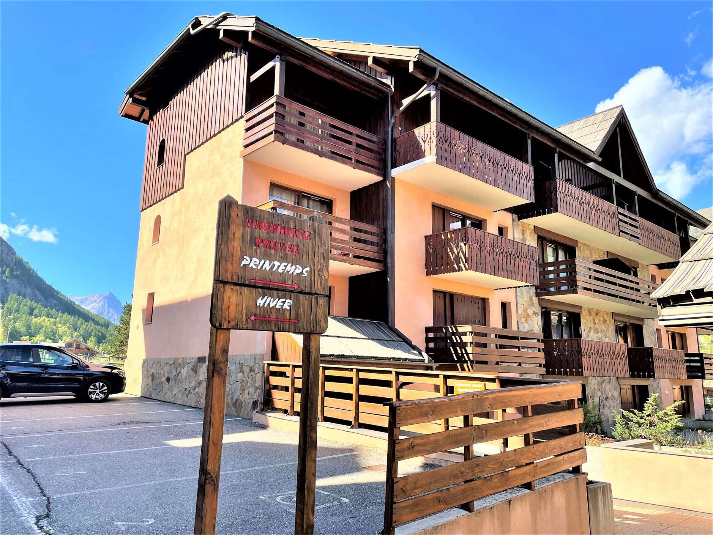 A wooden building with balconies, a sign indicating directions to 'Proprieta Privee' and 'Printemps', and a car parked in front.