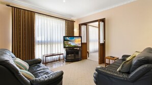 A living room with two leather sofas, a TV on a stand, and a door leading to another room. - Family Escape | Lakes Entrance Retreat (Lakes Entrance)