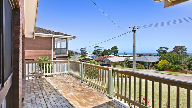 A residential balcony with a tiled floor and a white railing, overlooking a street with houses and a clear view of the ocean. - Family Escape | Lakes Entrance Retreat (Lakes Entrance)