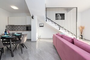 Una cocina moderna con armarios blancos, salpicadero de azulejos y un comedor con una mesa dispuesta para dos personas.