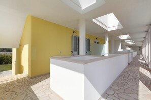 Un couloir avec un mur jaune, des colonnes blanches et un sol carrelé.