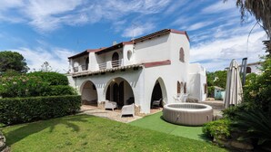A white building with arches and a red roof, surrounded by a well-maintained lawn and a hot tub.