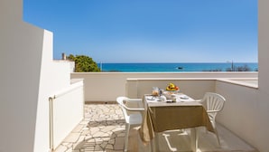 A balcony with a table set for two, overlooking a clear blue sea.