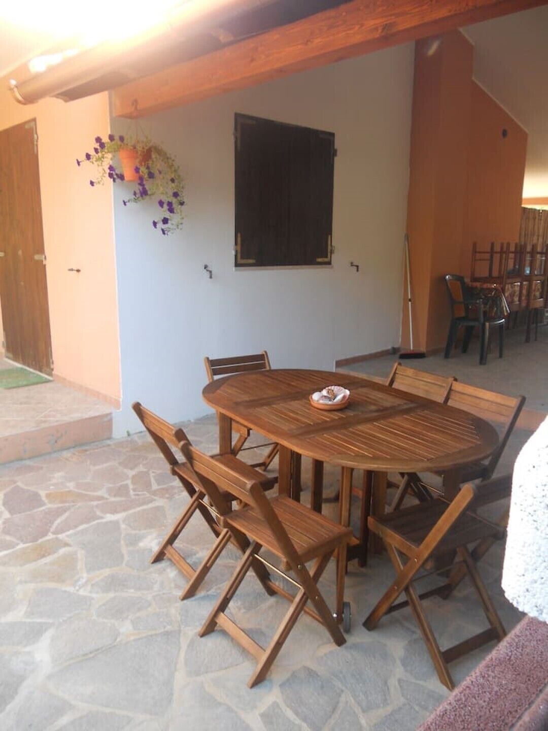 A wooden dining table with six chairs, a stone floor, and a hanging flower basket.