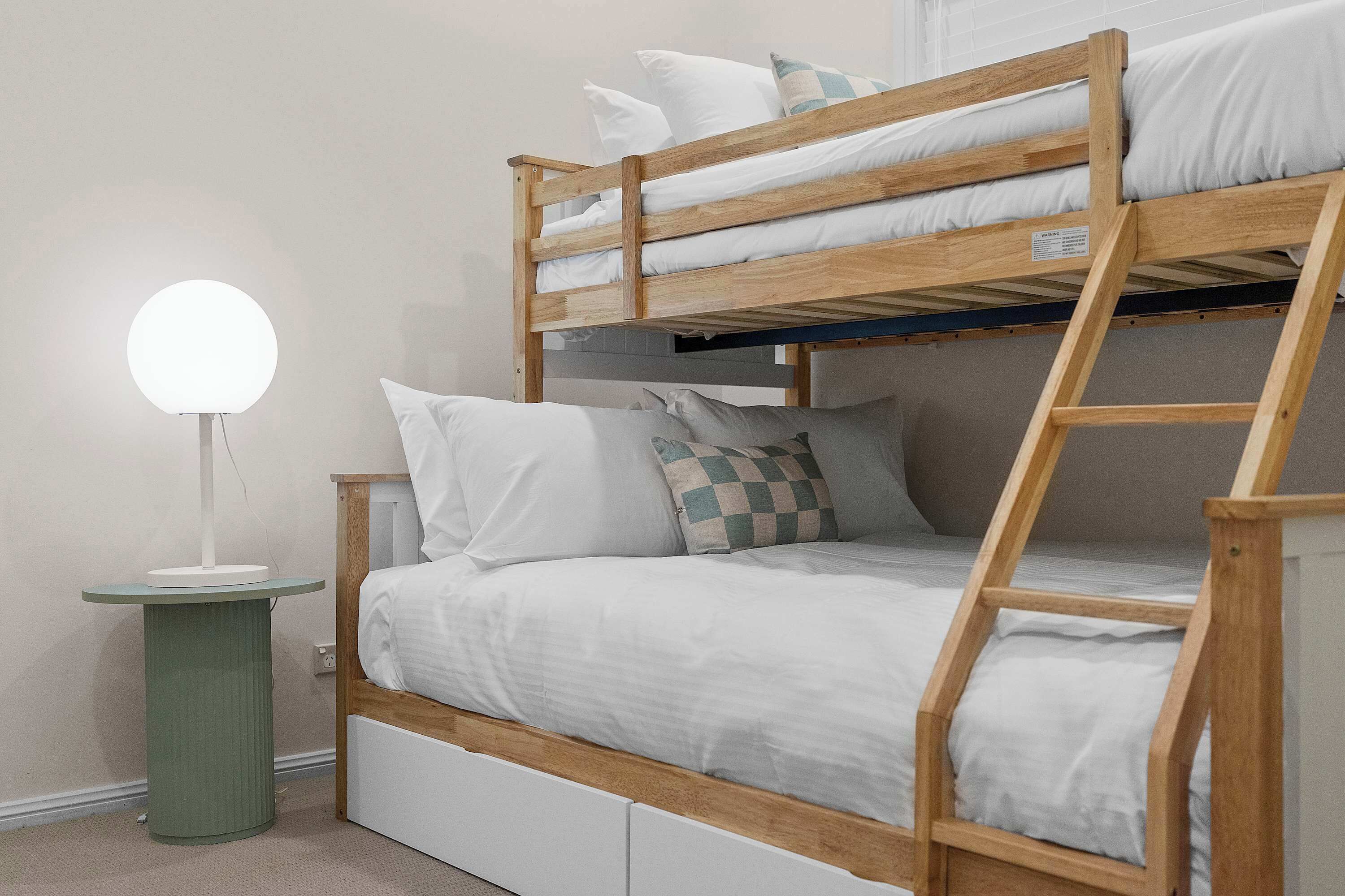 Un lit superposé avec une échelle, une table de chevet avec une lampe et un petit meuble à tiroirs.