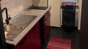 Een compacte keuken met een roestvrijstalen spoelbak, rode kastjes en een klein raam met blauw getint glas.