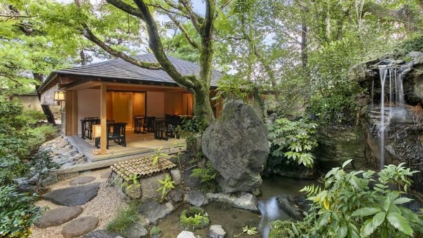 A traditional Japanese-style building with a wooden exterior, a stone pathway leading to a seating area, and a small waterfall feature. - Fufu Kyoto (Kyoto)