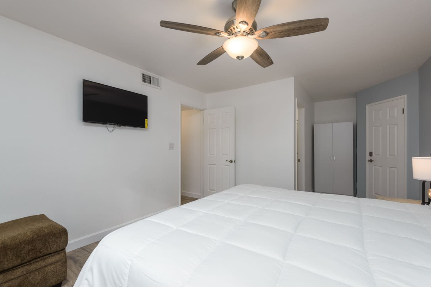 Un dormitorio con cama, ventilador de techo, televisión y puerta.