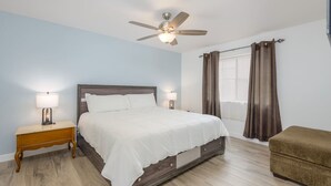 A bedroom with a bed, nightstands, a ceiling fan, a window with curtains, and a small seating area. - Walkable 2BR in Old Town w/ Pool + More (Scottsdale)