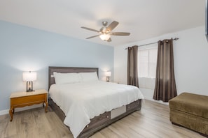 A bedroom with a bed, nightstands, a ceiling fan, a window with curtains, and a small seating area. - Walkable 2BR in Old Town w/ Pool + More (Scottsdale)