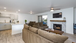 A modern living space with a kitchen, a seating area with sofas, a fireplace, and a flat-screen TV mounted on the wall. - Walkable 2BR in Old Town w/ Pool + More (Scottsdale)
