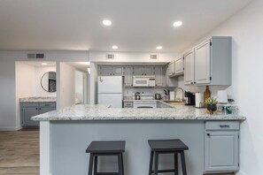 A modern kitchen with grey cabinets, a white refrigerator, a stove, and a marble countertop.