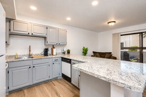 A modern kitchen with grey cabinets, a marble countertop, and a dishwasher.