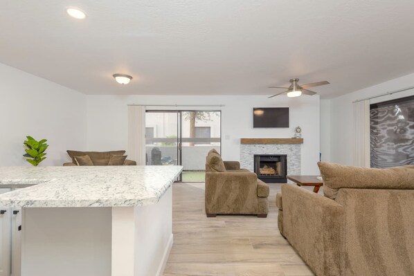 A modern living room with a fireplace, a large window, and a ceiling fan.