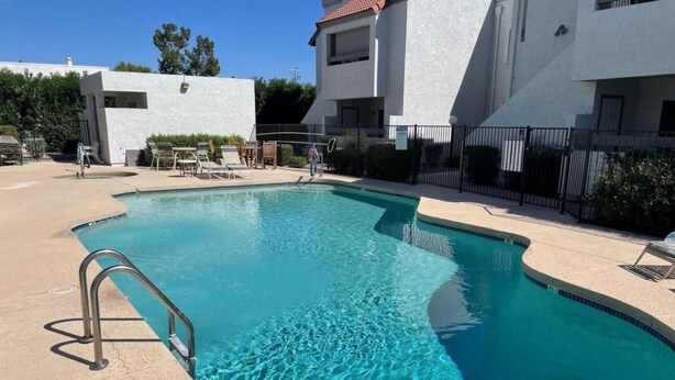 A swimming pool with a metal ladder, surrounded by a concrete deck and a fence. - Walkable 2BR in Old Town w/ Pool + More (Scottsdale)