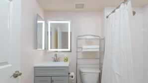 A bathroom with a toilet, a sink with a mirror, a towel rack, and a shower curtain. - Walkable 2BR in Old Town w/ Pool + More (Scottsdale)