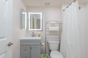 A bathroom with a toilet, a sink with a mirror, a towel rack, and a shower curtain. - Walkable 2BR in Old Town w/ Pool + More (Scottsdale)