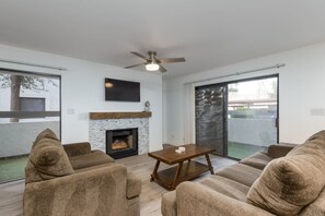 A modern living room with a fireplace, a ceiling fan, and a large sliding glass door to the outdoors.