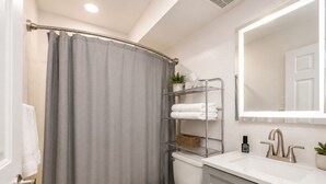 Une salle de bain avec un rideau de douche, des toilettes, un lavabo avec un miroir et une étagère avec des serviettes.