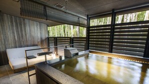 A spa area with a hot tub, a sofa, and a view of trees through large windows. - Fufu Nara (Nara)