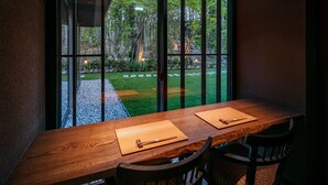 A dining area with a wooden table and chairs, large windows offering a view of a garden and trees. - Fufu Nara (Nara)