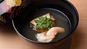 A bowl of soup with a shrimp and a piece of fish, garnished with parsley, on a wooden table.