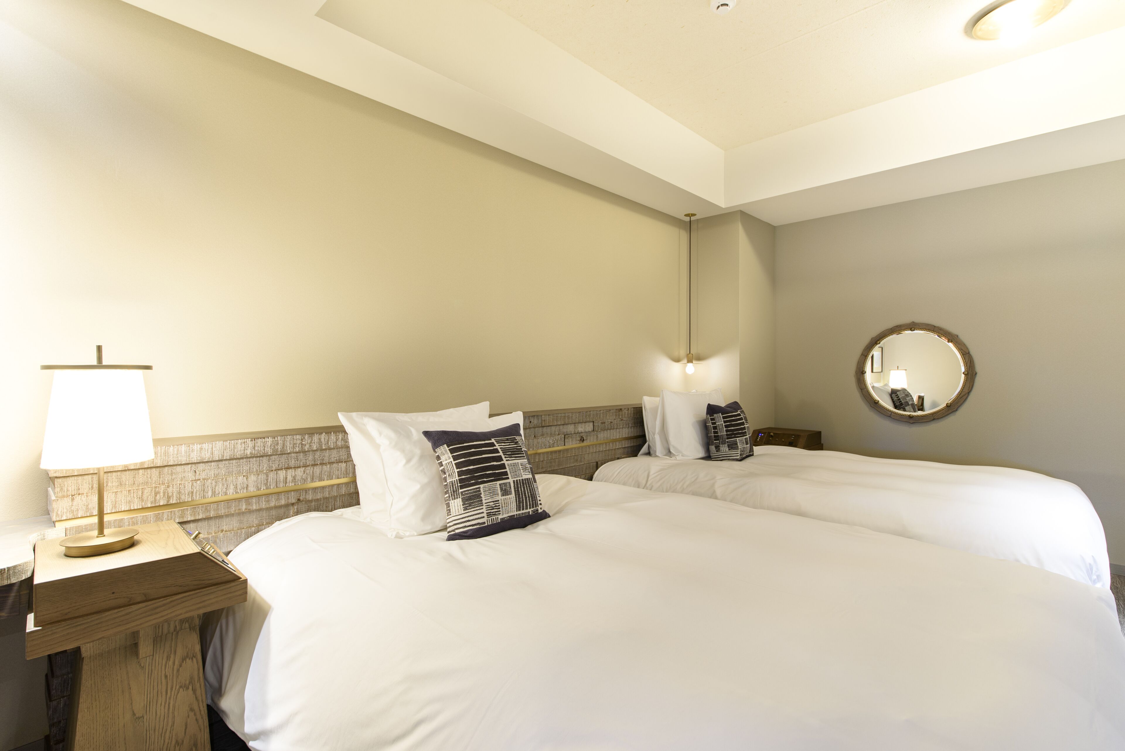 A hotel room with two beds, a nightstand with a lamp, a mirror, and a wooden headboard.