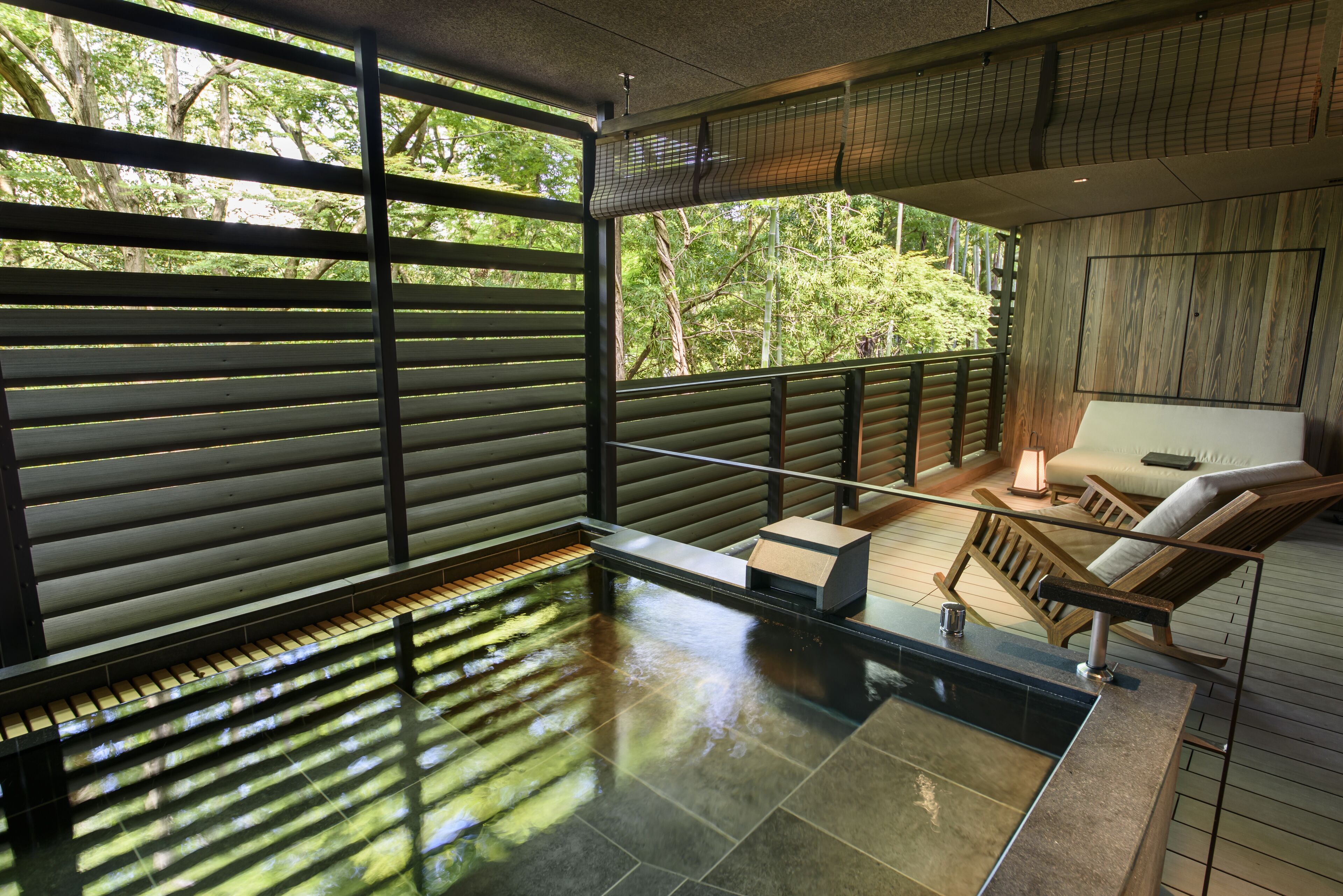 A modern spa area with a glass-enclosed hot tub, wooden deck, and seating area with a view of trees.