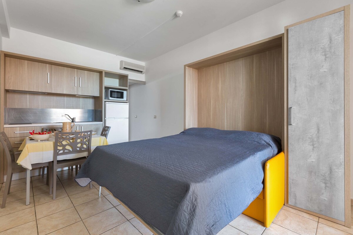 A compact bedroom with a bed, a small kitchenette, and a dining area.