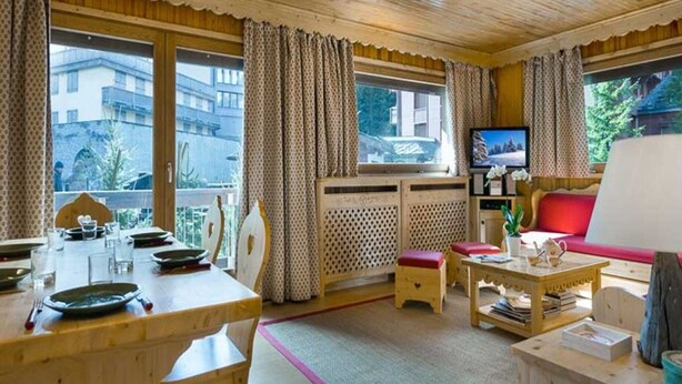 Une pièce chaleureuse avec un plafond en bois, une table à manger avec des chaises, un canapé, un téléviseur et une fenêtre avec des rideaux.