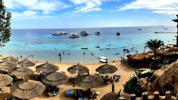 A beach with thatched umbrellas, a sandy shore, and several boats in the water. - Faraana Reef - All-inclusive (Sharm El Sheikh)