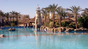 A clear blue pool with a lighthouse structure in the background, surrounded by palm trees and buildings. - Faraana Reef - All-inclusive (Sharm El Sheikh)