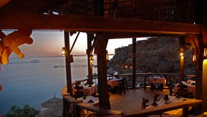 An outdoor restaurant with tables and chairs, overlooking a body of water and a rocky cliff. - Faraana Reef - All-inclusive (Sharm El Sheikh)