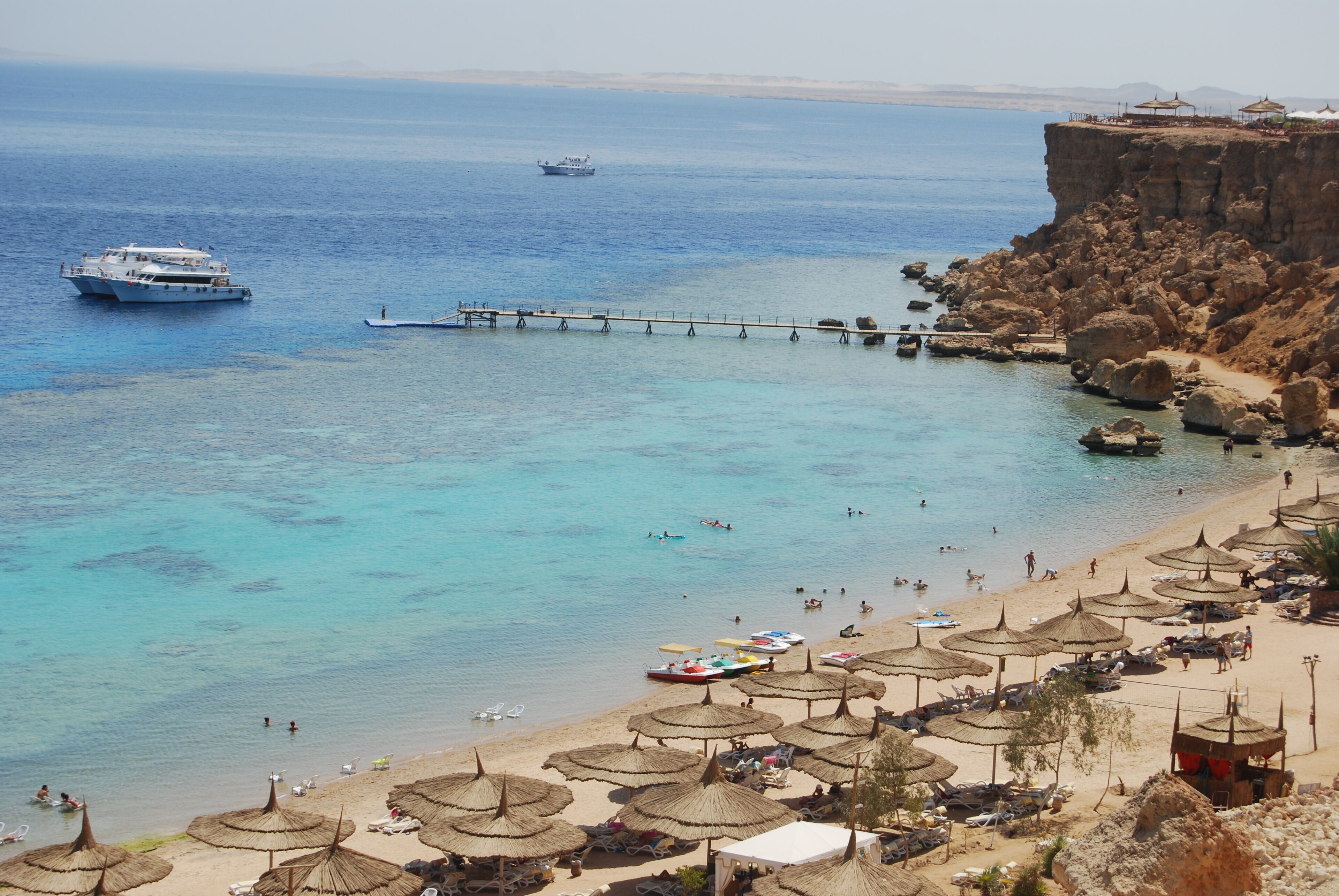 A beach with clear blue water, a pier, and umbrellas.