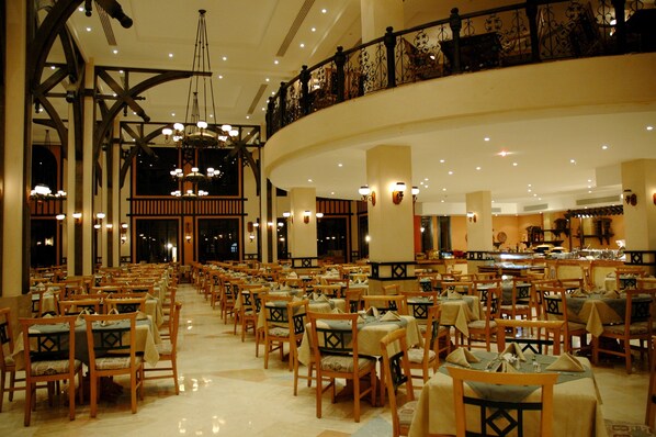 A spacious dining area with multiple tables and chairs, a high ceiling with chandeliers, and a balcony with ornate railings. - Faraana Reef - All-inclusive (Sharm El Sheikh)