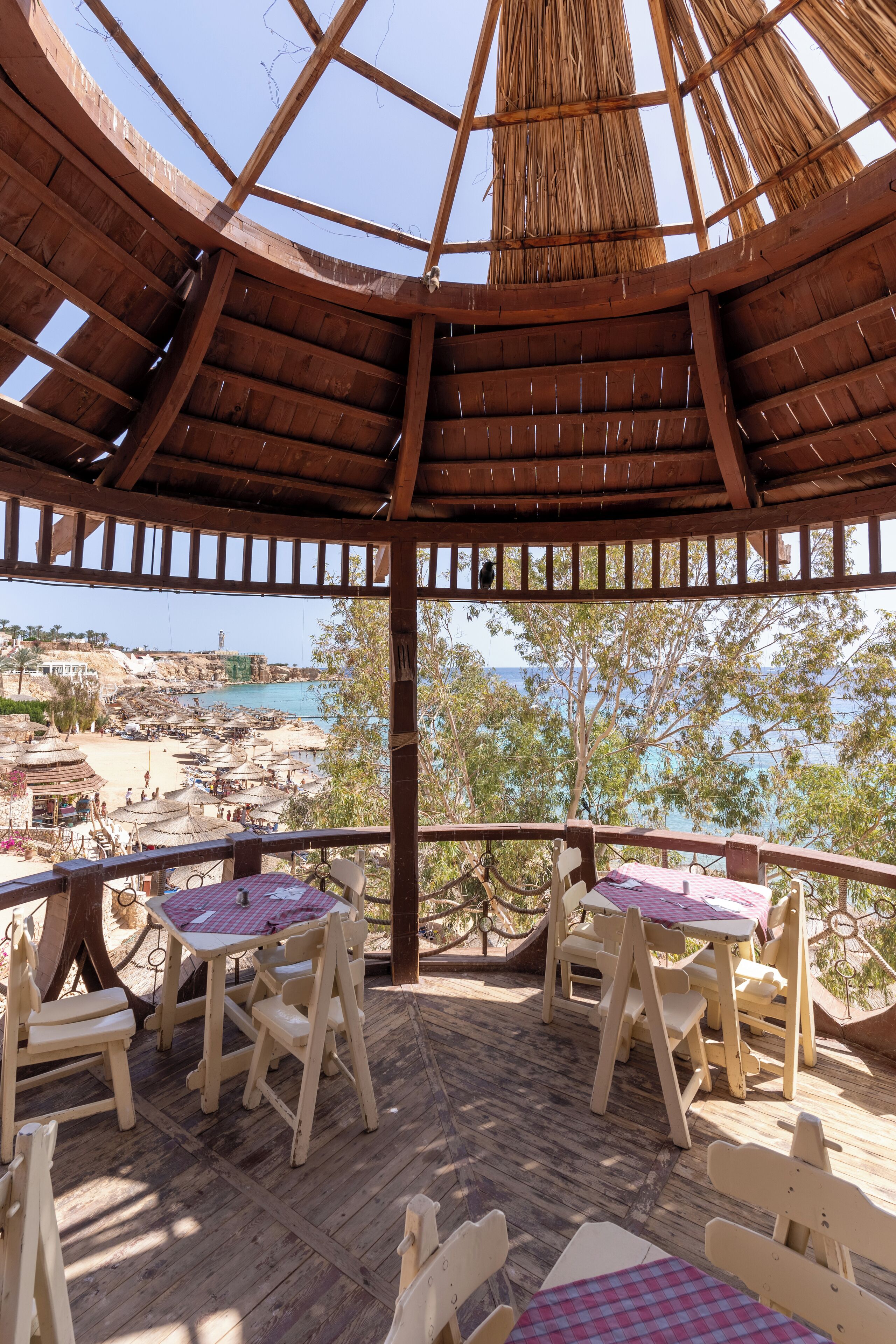 A wooden gazebo with a thatched roof overlooking a beach.
