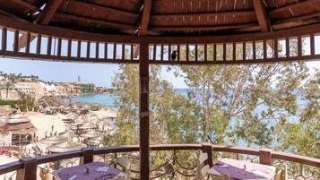A wooden gazebo with a thatched roof overlooking a beach.
