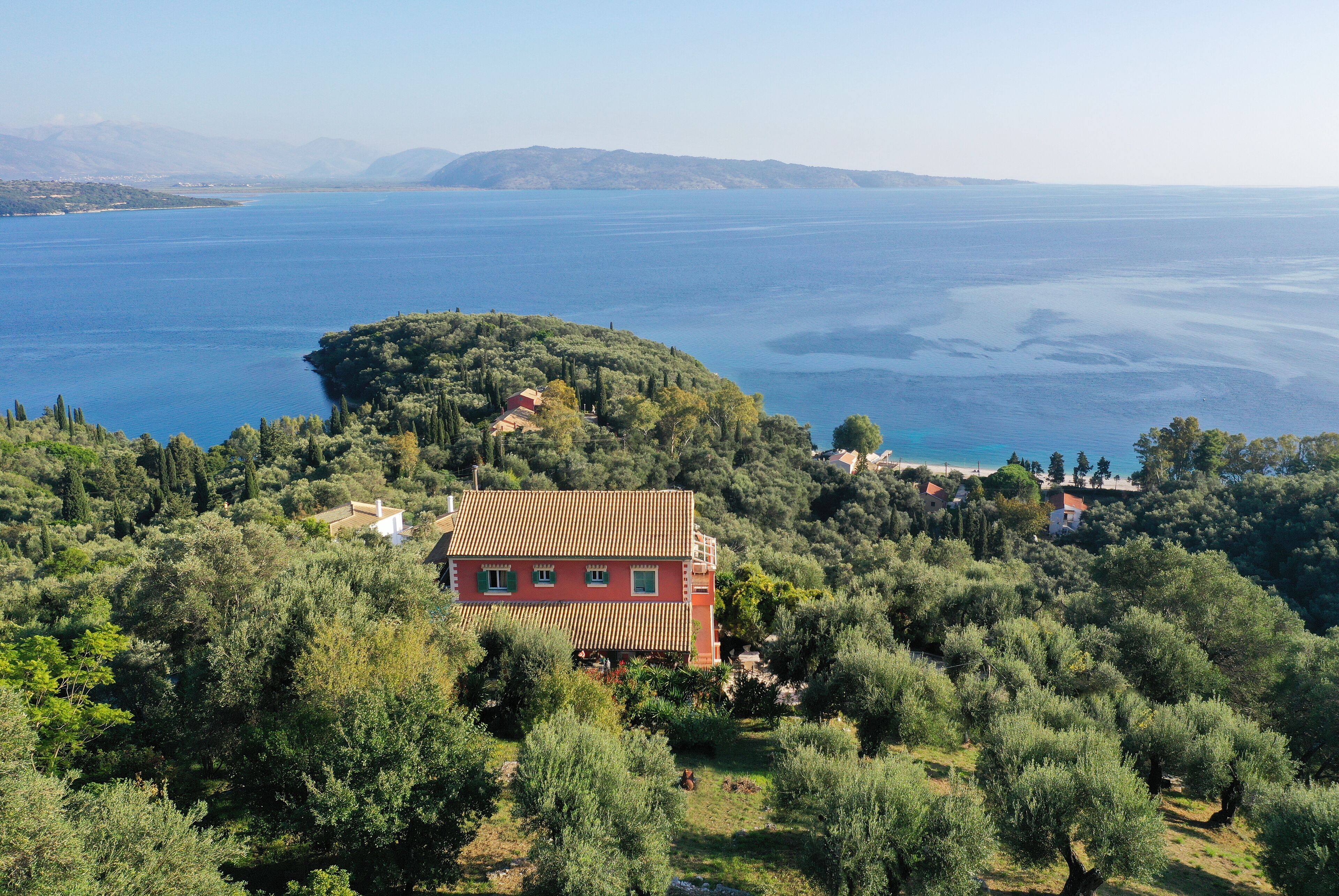 A coastal property with a large house surrounded by dense vegetation and a view of the sea.