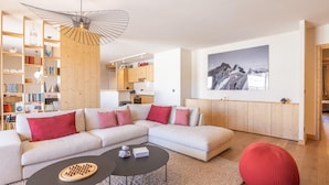En moderne stue med en hjørnesofa, et sofabord, en rød puf og en reol.
