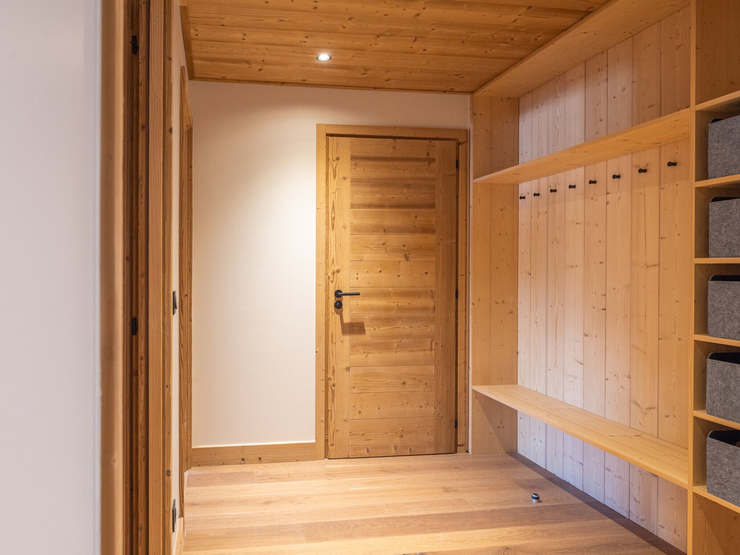 Een kamer met houten lambrisering, een deur, planken en een klein tafeltje.