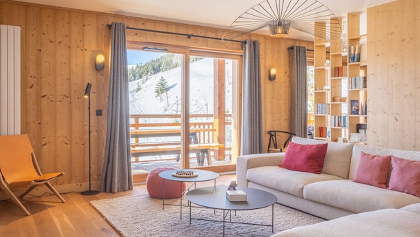 En hyggelig stue med sofa, skammel og sofabord, trævægge og en reol.