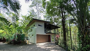 Ein zweistöckiges Haus mit Garage, umgeben von dichter tropischer Vegetation.