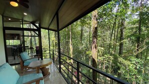 Ein Balkon mit Blick auf einen dichten Wald. Ein Tisch und zwei Stühle mit Kissen sind vorhanden.