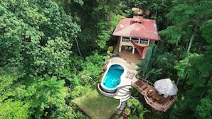 Vista aérea de una casa rodeada de bosque frondoso, con piscina y terraza de madera.