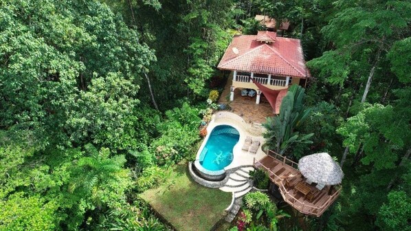 Eine Luftaufnahme eines Hauses, umgeben von dichtem Wald, mit Swimmingpool und Holzterrasse.