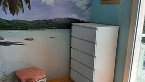 Ein Zimmer mit einem Meereswandbild, einem weißen Schrank und einem rosafarbenen Sitzhocker.