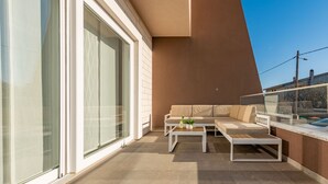 Un área de estar moderna al aire libre con sofá, mesa de centro, ventanas amplias y una vista despejada del cielo.