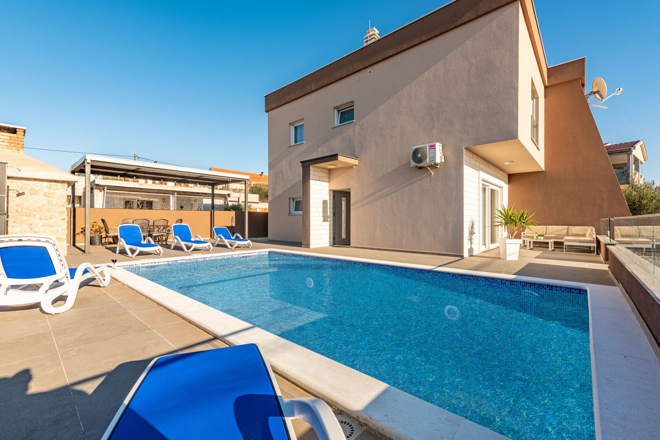 A modern building with a swimming pool, lounge chairs, and a covered patio area.